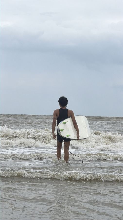 A student walking into the sea with a surfboard